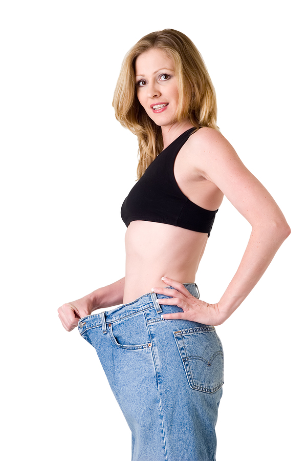 Attractive slim blond woman demonstrating weight loss by wearing an old pair of jeans and holding out to show how big the pants are, lipo b injections