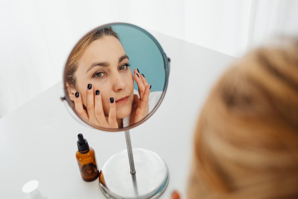 woman's reflection in a mirror applying skincare products aha vs bha